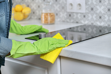 Woman hands in gloves washing and cleaning electric hob in kitchen